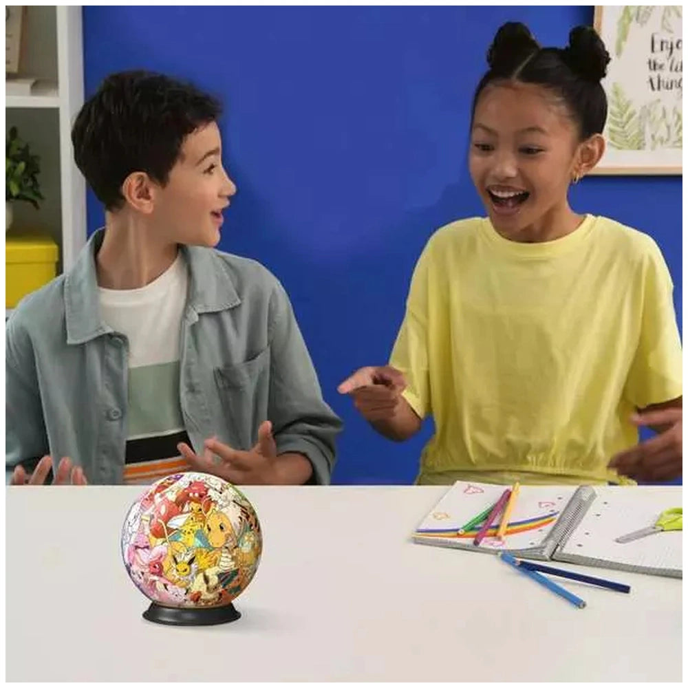 Ravensburger 3D-Puzzle-Ball featuring Pokémon characters is displayed on a table as two children engage in a creative activit
