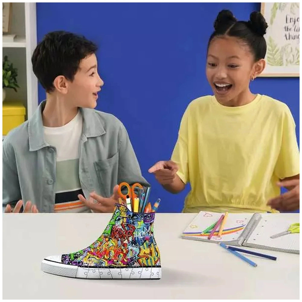 Ravensburger 3D puzzle sneaker figures are showcased as two children engage joyfully at a table filled with art supplies.