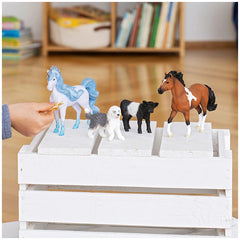 Flowy Unicorn Mare figurine alongside three colorful horse figurines and a dog on a white platform atop a wooden floor.