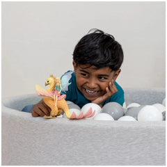 Schleich Phoenix toy held by a smiling child in a white ball pit filled with white balls, wearing a blue top.