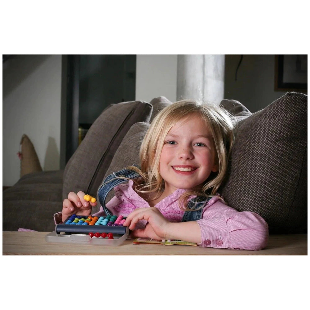 A young girl with blonde hair in a pink shirt smiles while engaged with a small keyboard on a textured couch.
