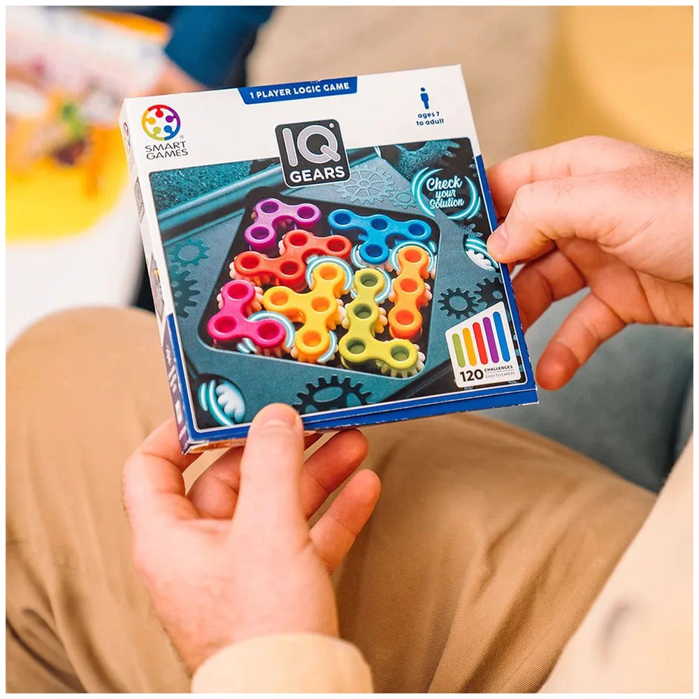 Smart Games IQ Gears box held by hands, featuring colorful designs and a gears graphic, suitable for ages 7 and up.