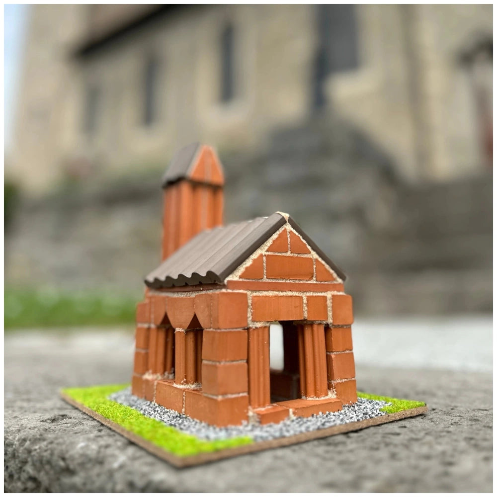 Teifoc Church model made of red bricks with a corrugated metal roof, set on a green base in an urban outdoor setting.