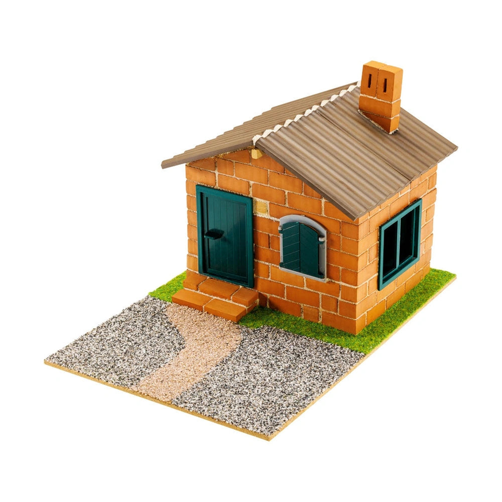 Teifoc house model features an orange brick facade, green door and windows, gray roof, on a grass-textured base with gravel p