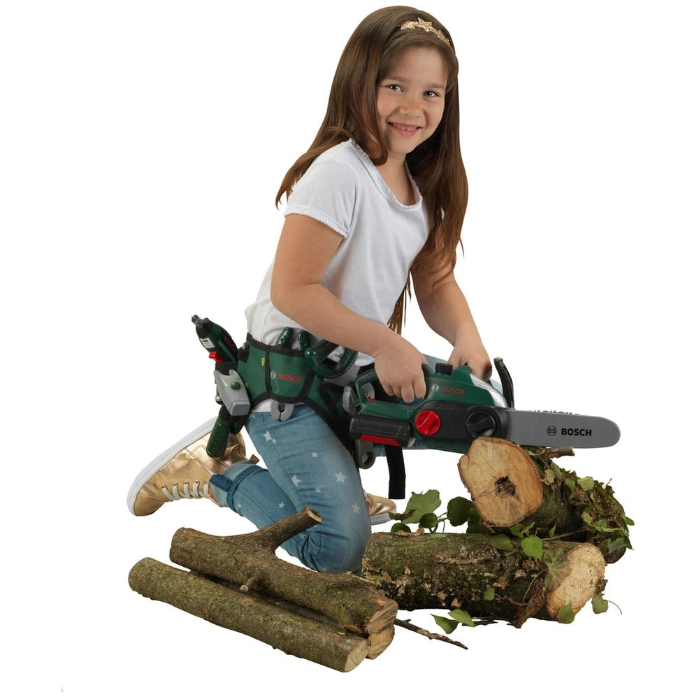 Theo Klein Bosch chainsaw toy held by a girl in a white t-shirt and blue jeans, standing on a mossy log.