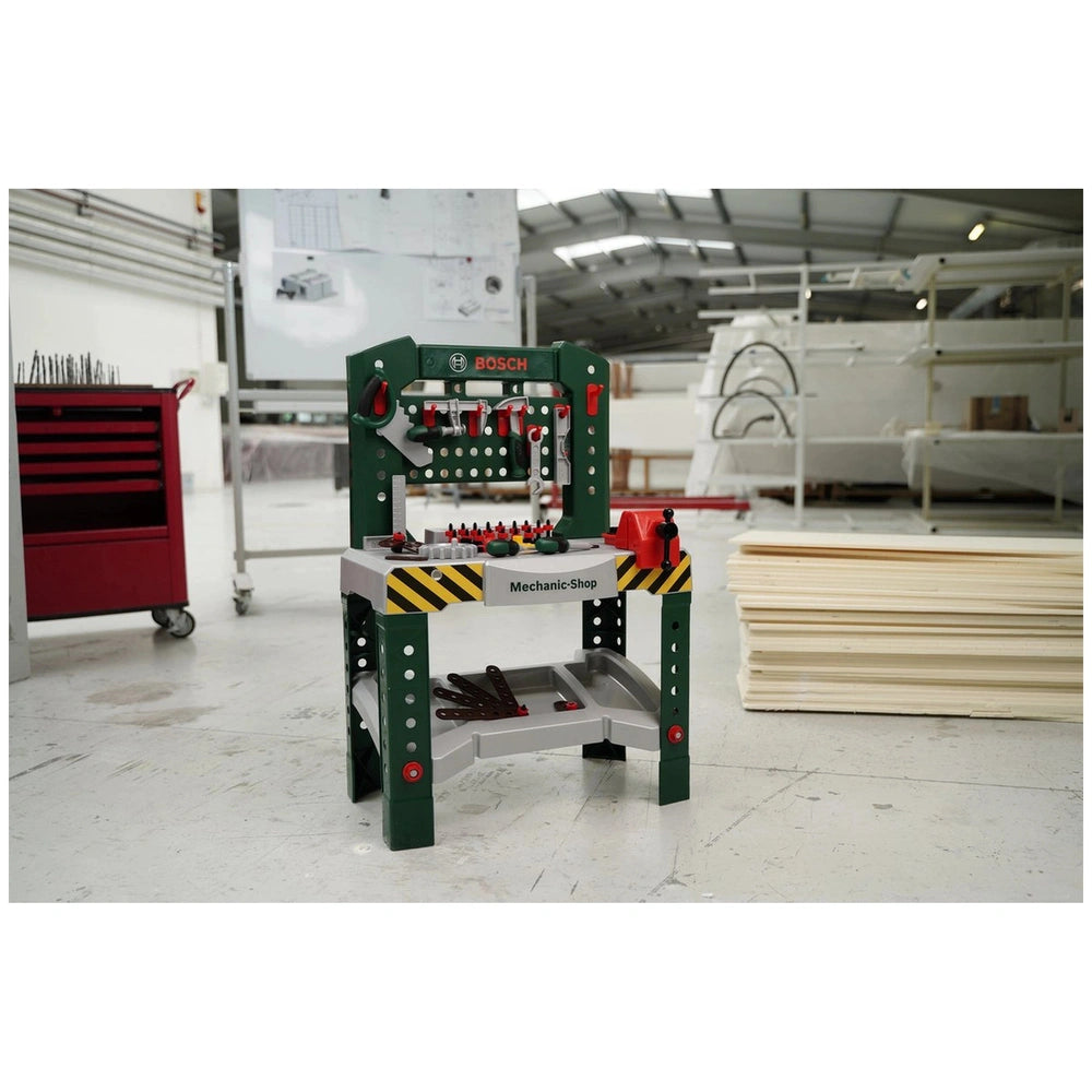 Theo Klein Bosch workbench features a green metal base with yellow and black striped top, red buttons, levers, and switches.